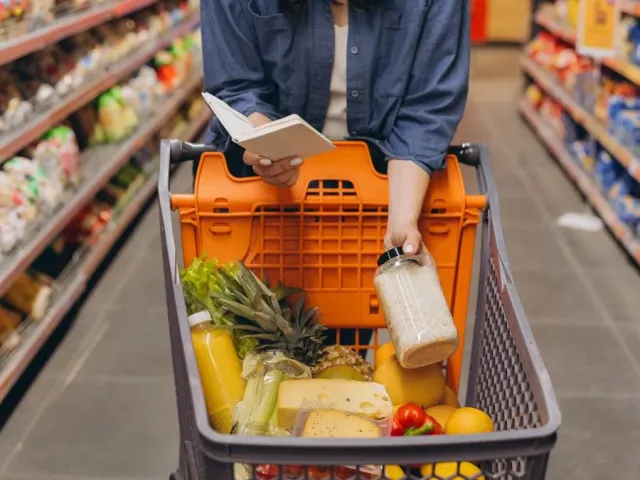 Lista de compras na mão, sobre o carrinho cheio no mercado