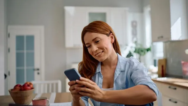 Mulher na cozinha olhando o celular com o e-mail de acesso recem-chegado